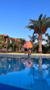 a woman standing next to a swimming pool with a palm tree at Tropic Hôtel in Rivesaltes