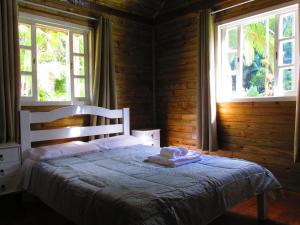 a bedroom with a white bed with two windows at Refúgio dos Valdenses in Morretes