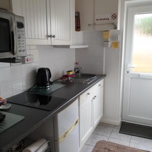 a kitchen with white cabinets and a black counter top at Beachfront Studio in Pevensey