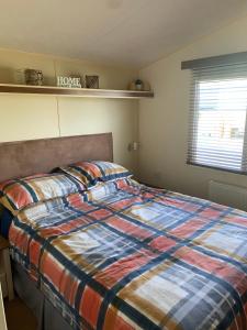 een slaapkamer met een bed met een geruite deken bij Thornwick Bay Haven Site-Large Homely Static Caravan, Sun, Sea And Sand (SEA VEIWS , LIGHTHOUSE VEIWS) in Flamborough