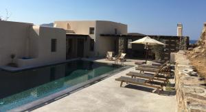 a house with a swimming pool with chairs and an umbrella at Aviola Mykonos in Ftelia