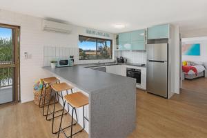 a kitchen with a counter with stools and a refrigerator at CANAL7-ON THE MOOLOOLABA CANAL! in Mooloolaba