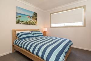 1 dormitorio con cama de rayas azul y blanco y ventana en Happy Daze, en Smiths Lake