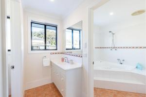 a white bathroom with a sink and a tub at Akoya House 122 Tomaree Rd Pet friendly linen air conditioning WiFi and boat parking in Shoal Bay +32 photos