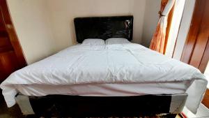 - un lit avec des draps blancs et une tête de lit noire dans une chambre dans l'établissement Homestay Merpati Dieng Syariah RedPartner, à Diyeng