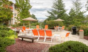 un patio con sillas naranjas, mesas y sombrillas en Ashland Hills Hotel & Suites en Ashland