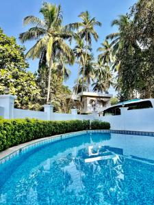 a swimming pool in front of a house with palm trees at Arotel Rooms & Suites in Calangute