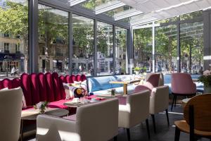 un restaurante con sillas rojas, mesas y ventanas en Hôtel Nude Paris - Color Vision, en París