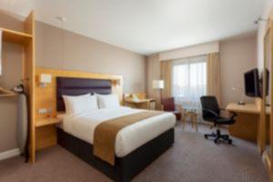 Cette chambre comprend un lit, un bureau et une télévision. dans l'établissement Holiday Inn London Brentford Lock, an IHG Hotel, à Brentford