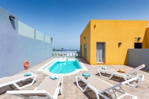 a swimming pool with lounge chairs and a yellow building at Villa Horizon in Caleta De Fuste