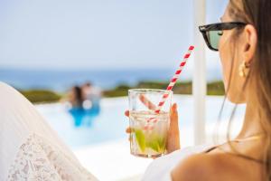 a woman wearing sunglasses holding a drink on the beach at Vila Maria Hotel - Adults Only in Albufeira