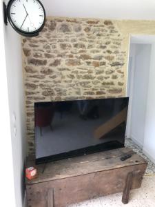 a flat screen tv sitting against a stone wall with a clock at Gîte Le Coq Au Vert en Suisse Normande in Hamars