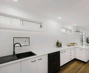una cocina con armarios blancos y fregadero negro en Lakeview House LILAC, en Chittaway Point