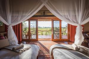 a bedroom with two beds and a view of a patio at Amber River Camp in Okavango Delta