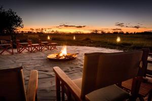 a fire pit on a patio with chairs and a sunset at Amber River Camp in Okavango Delta