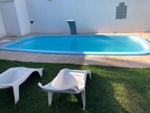 a swimming pool with two white chairs in the grass at Diversão, férias, casa na praia de cumbuco. in Caucaia