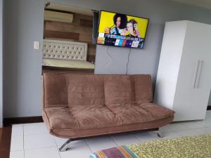 ein Sofa im Wohnzimmer mit einem TV an der Wand in der Unterkunft Villas do Pratagy Com Jacuzzy Prive Bromelia 301 in Maceió