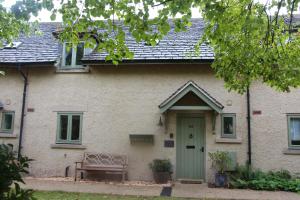 uma casa com uma porta verde e um banco em Coot Cottage em Somerford Keynes