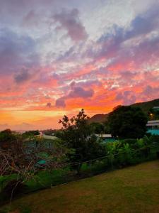 einen Sonnenuntergang über einem Feld mit einem Zaun und Bäumen in der Unterkunft Juju's Cottage with magnificent views in Laborie