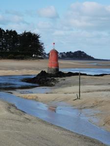 a red lighthouse sitting on a beach near the water at Chambres d'Hôtes vue mer entre Plestin les Grèves et locquirec in Plestin-les-Grèves