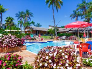a swimming pool with flowers and a red umbrella at Caldas Park e Hotel - Caldas Novas in Caldas Novas