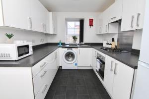 a white kitchen with a washing machine and a microwave at Serene 7Bed Escape - Steps from Coventry City Center, Holiday Bliss! in Coventry
