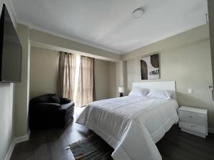 a bedroom with a white bed and a black chair at Departamentos Caraz in Caraz