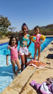 dwie dziewczyny i chłopiec stojący obok basenu w obiekcie Estância Morro Do Frota w mieście Pirenópolis