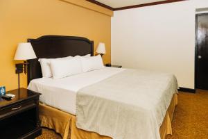 una habitación de hotel con una cama grande con sábanas blancas en Plaza Hotel and Suites, en San Salvador