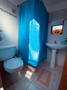 baño con aseo y lavamanos con cortina de ducha azul en Hostal Katari, en San Pedro de Atacama