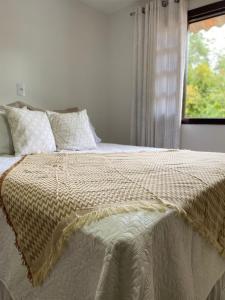 a bed with a white comforter and a window at Sitio do Marinho em Nova Trento in Nova Trento