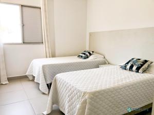 1 dormitorio con 2 camas con sábanas blancas y ventana en Apartamento da Pitangueiras, en Guarujá