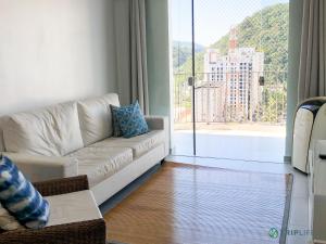 a living room with a white couch and a large window at Apartamento da Pitangueiras in Guarujá