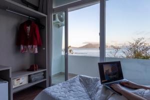 a person sitting on a bed with a laptop in front of a window at Marambaia Hotel e Convenções in Balneário Camboriú