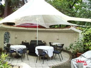 eine Terrasse mit Tischen, Stühlen und einem Sonnenschirm in der Unterkunft L'Auberge in Walldorf