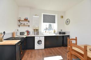 a kitchen with black cabinets and a washer and dryer at The John Muir - Beautiful 1 bed apartment in Helensburgh in Helensburgh