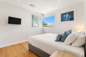 1 dormitorio blanco con 1 cama y TV en Ocean Sapphire, en Byron Bay