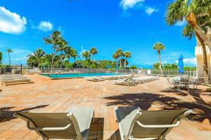 a patio with chairs and a swimming pool with palm trees at Cozy beachfront condo with pool and tennis courts in Marco Island