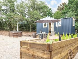 um pátio com um guarda-sol e uma mesa com uma cadeira em High Grounds Shepherd's Hut em Ashbourne