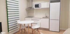 eine kleine Küche mit einem Tisch und weißen Stühlen in der Unterkunft Apartamentos Ilustración in Albacete