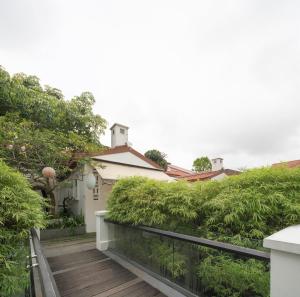 einen Holzsteg, der zu einem Haus mit grünen Büschen führt in der Unterkunft The Sultan in Singapur