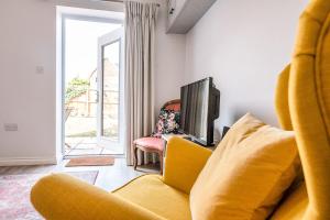 a living room with a yellow couch and a tv at Martlet Cottage Aldeburgh Air Manage Suffolk in Aldeburgh