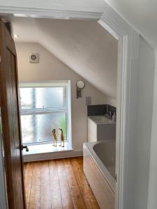 un baño con bañera y un perro sentado en una ventana en Fig Cottage Holiday Home en Whitecroft