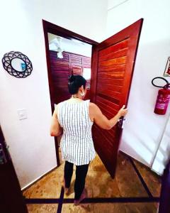 a woman opening a wooden door in a room at Residencial Bem-te-vi in Jericoacoara