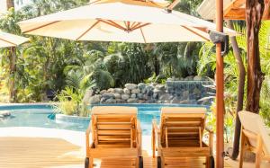 two chairs and an umbrella next to a swimming pool at Hotel Guiones in Nosara