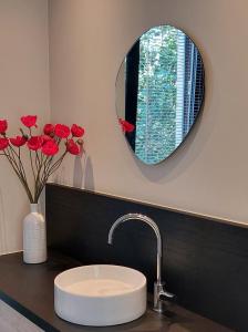 La salle de bains est pourvue d'un lavabo, d'un miroir et de roses rouges. dans l'établissement Geniet van alle comfort tussen Ieper en Heuvelland, à Ypres