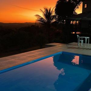 a blue swimming pool with a sunset in the background at Casa da Vista - LAGOA SANTA in Lagoa Santa