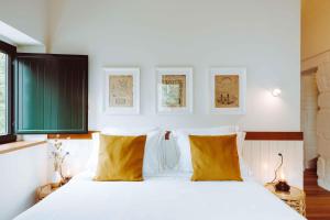 um quarto com uma cama com lençóis brancos e almofadas amarelas em Oliveiras Village — Agroturismo em Amarante mais 37 fotografias