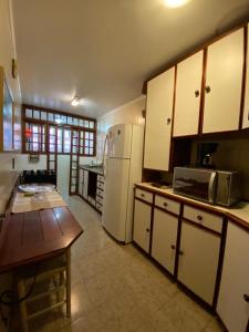 a kitchen with white cabinets and a table and a refrigerator at Apartamento Alto da Serra - 024 in Gramado