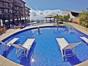 a large swimming pool with chairs and a woman in the water at Apartamento em Barra Bali, Resort de Luxo - Destino BSM 329 in Barra de São Miguel